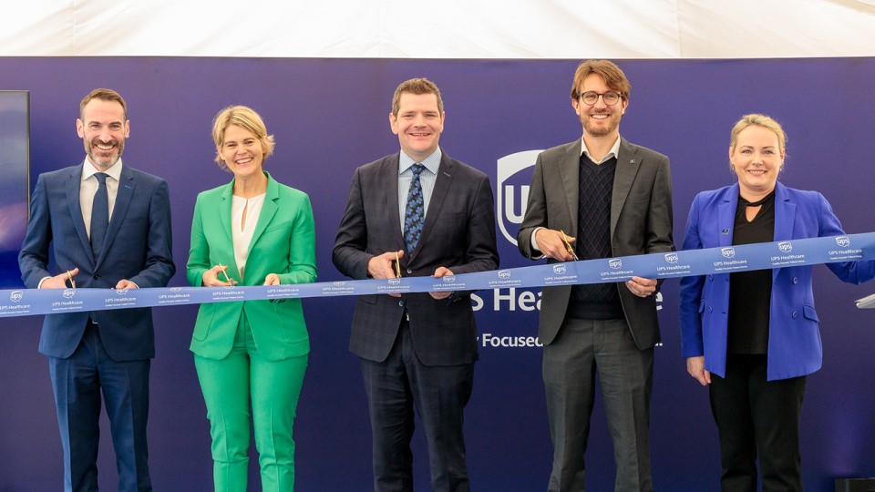 Five business professionals cutting a grand opening ribbon together.