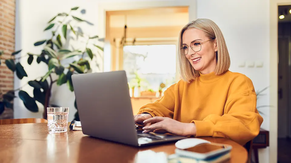 a person wearing an orange sweater sitting at a table on their computer