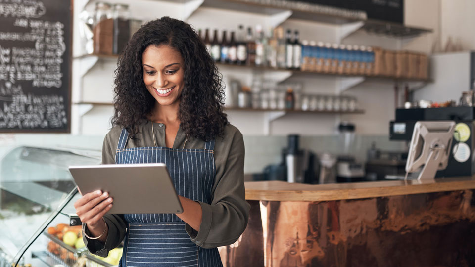 Smiling woman working in restaurant using tablet to see UPS My Choice dashboard