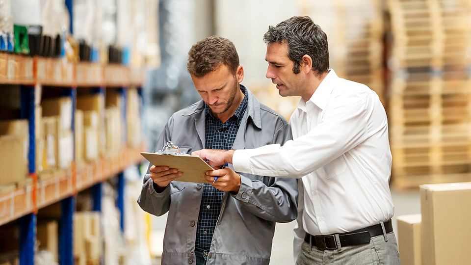 Two men look at clipboard in warehouse